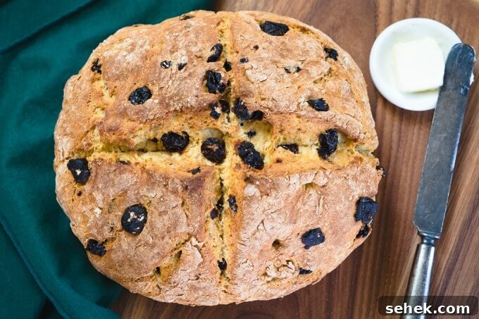 Dutch Oven Cherry Irish Soda Bread Recipe 2 Top-down view of a whole loaf of Soda Bread dotted with cherries over a green napkin on a wooden cutting board.