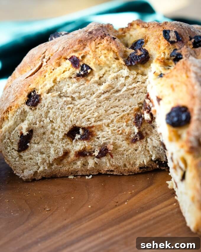 Dutch Oven Cherry Irish Soda Bread Recipe 6 Front view of a loaf of Soda Bread dotted with cherries with a wedge removed next to a green napkin on a wooden cutting board.