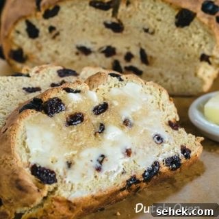 Dutch Oven Cherry Irish Soda Bread Recipe 7 Level view of slices of soda bread dotted with raisins sitting on a wooden cutting bread. Butter is melting down the slice and a white bowl of butter sits to the side.