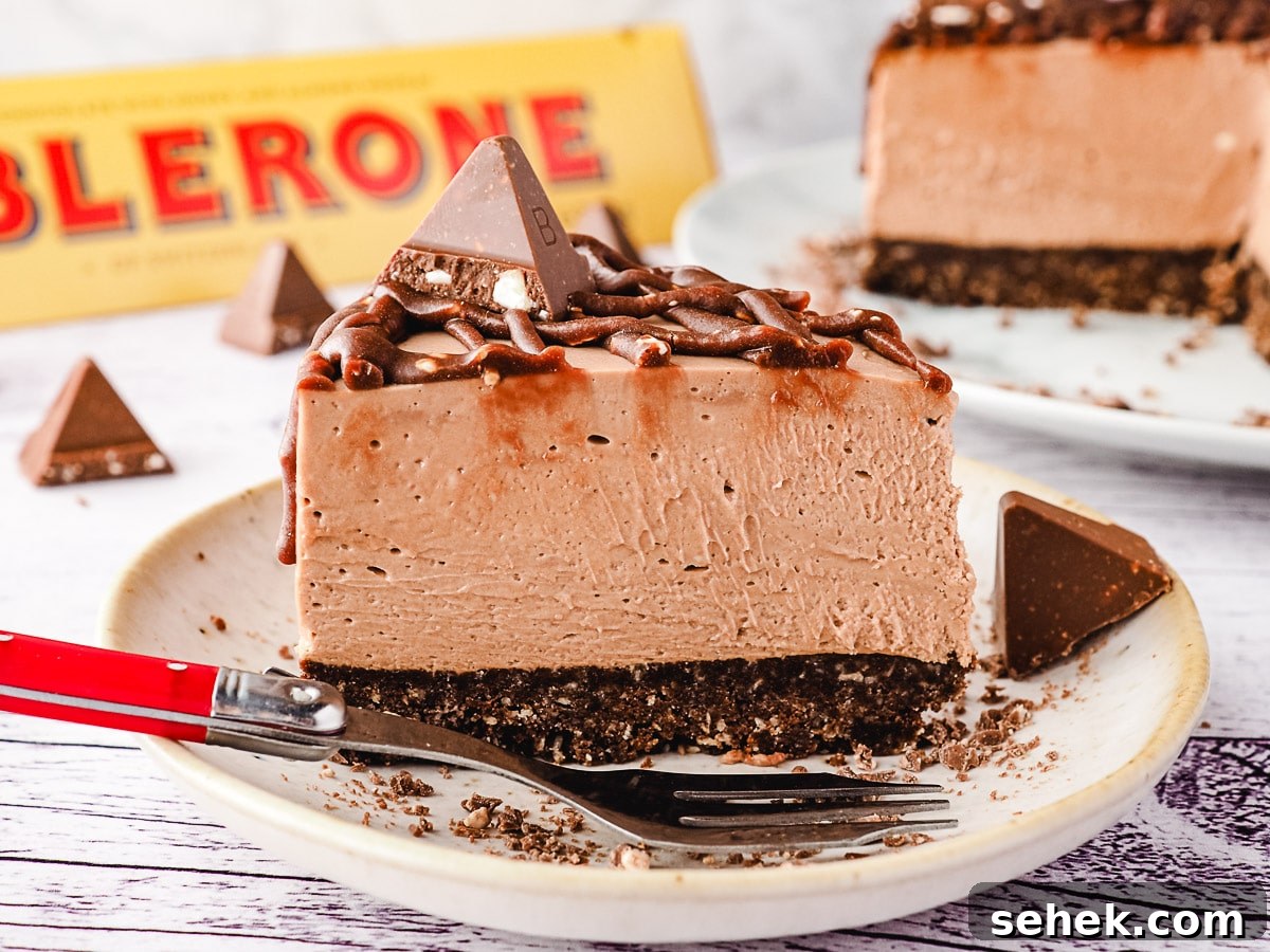 Decadent Toblerone Cheesecake Recipe with Crunchy Chocolate Honeycomb 2 Slice of Toblerone cheesecake on a plate, with rest of cheesecake and more Toblerone in background.