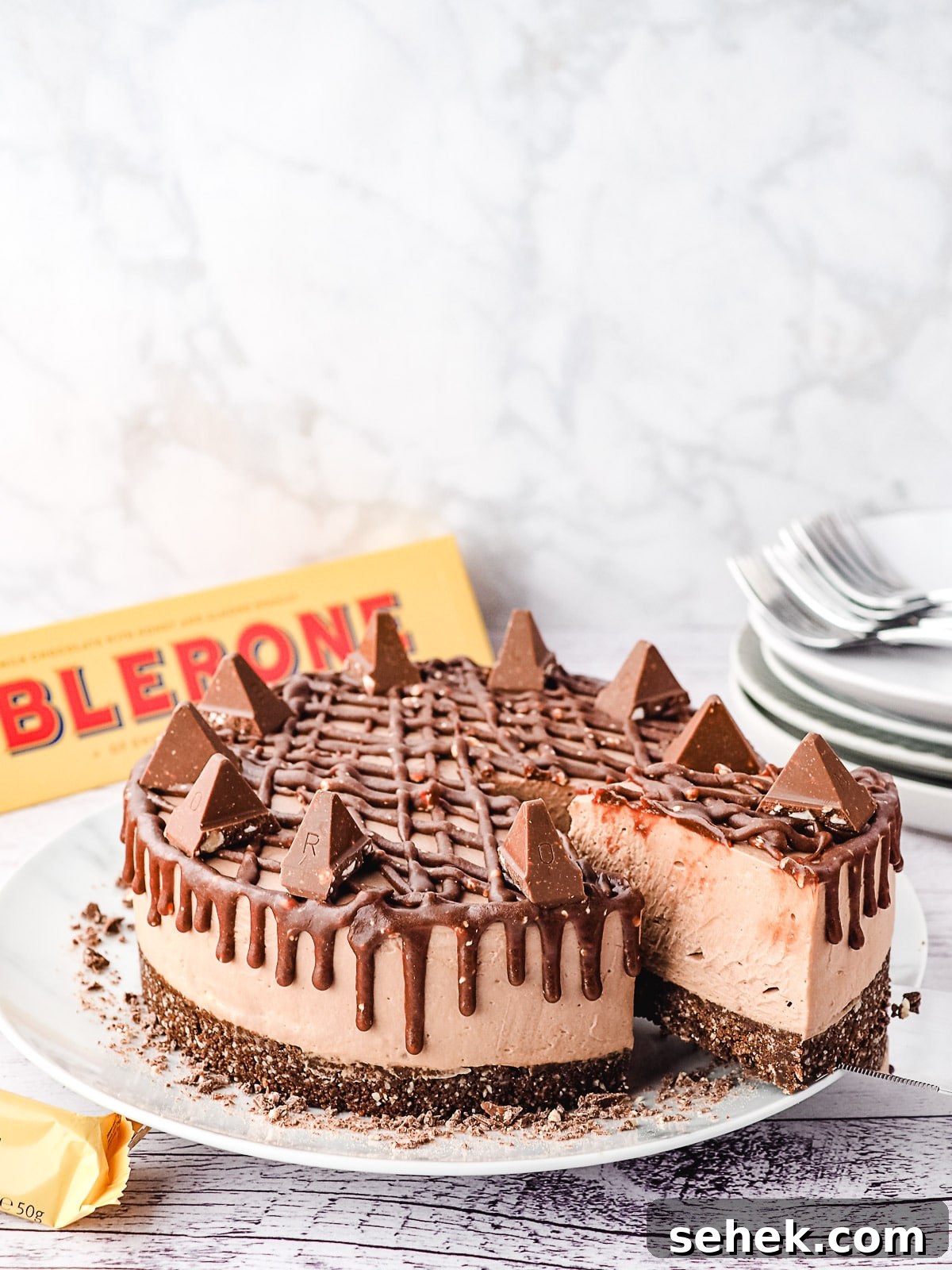 Decadent Toblerone Cheesecake Recipe with Crunchy Chocolate Honeycomb 13 Slicing cheesecake, with plate and Toblerone in the background.