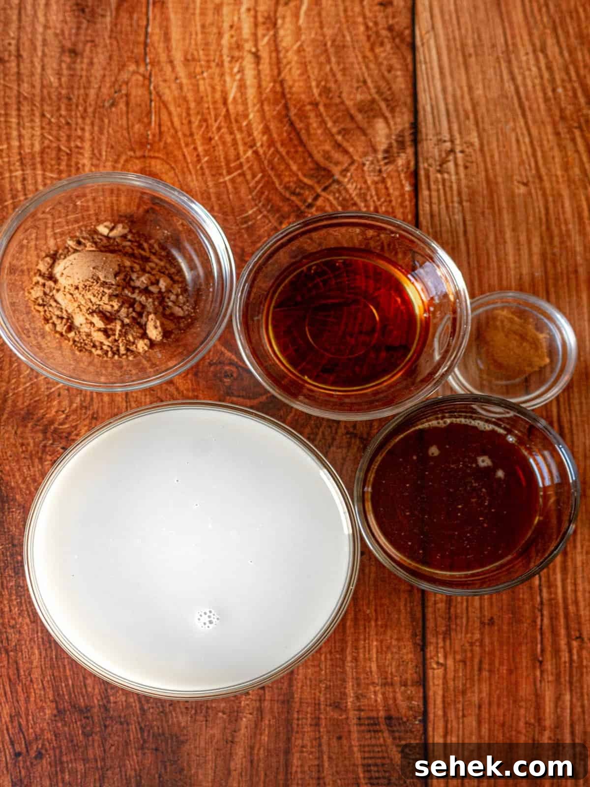 Dairy-Free Spiked Hot Chocolate Recipe: Cozy Vegan Cocoa with Rum 3 Clear bowls filled with milk, syrup, bourbon, cinnamon and cocoa powder.