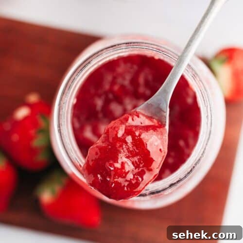 A mason jar with strawberry filling for cake with a silver spoon.