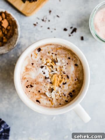 Toasted coconut hot chocolate in a mug topped with coconut cream, toasted coconut, and chocolate shavings.