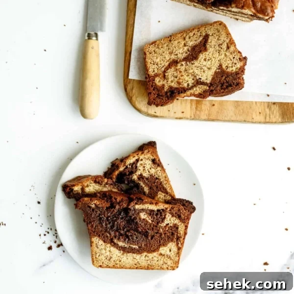 Two slices of a marbled loaf cake on a white plate, with more slices and a knife on a wooden cutting board nearby. Crumbs are scattered on the white surface.