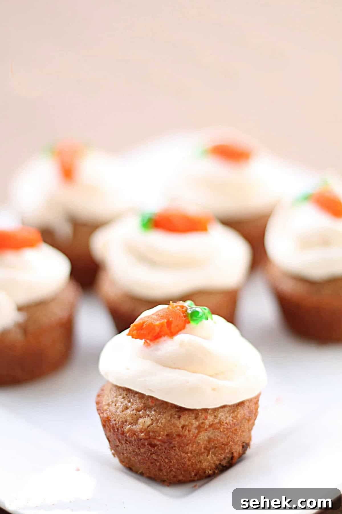 A close-up of mini cupcakes with white frosting and small orange and green decorations on top, arranged on a white plate.