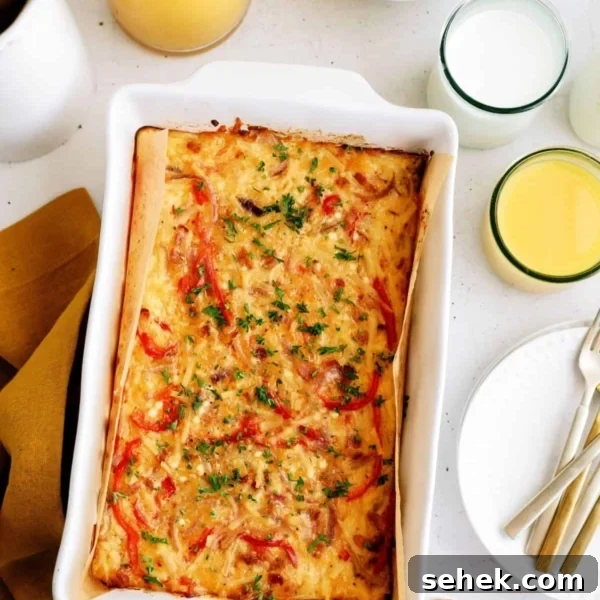 Baked casserole with red peppers and herbs in a white dish, surrounded by eggs, apples, orange juice, and a glass of milk on a table.