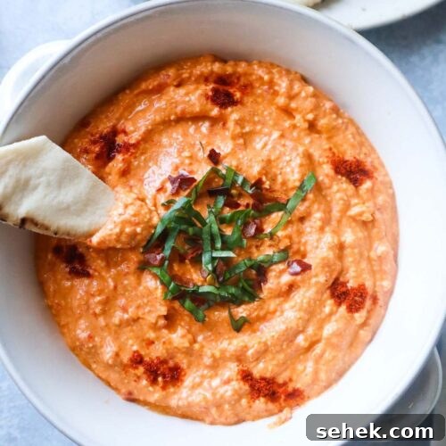 white bowl with paprika dip topped with fresh basil and paprika with pita chip sticking out