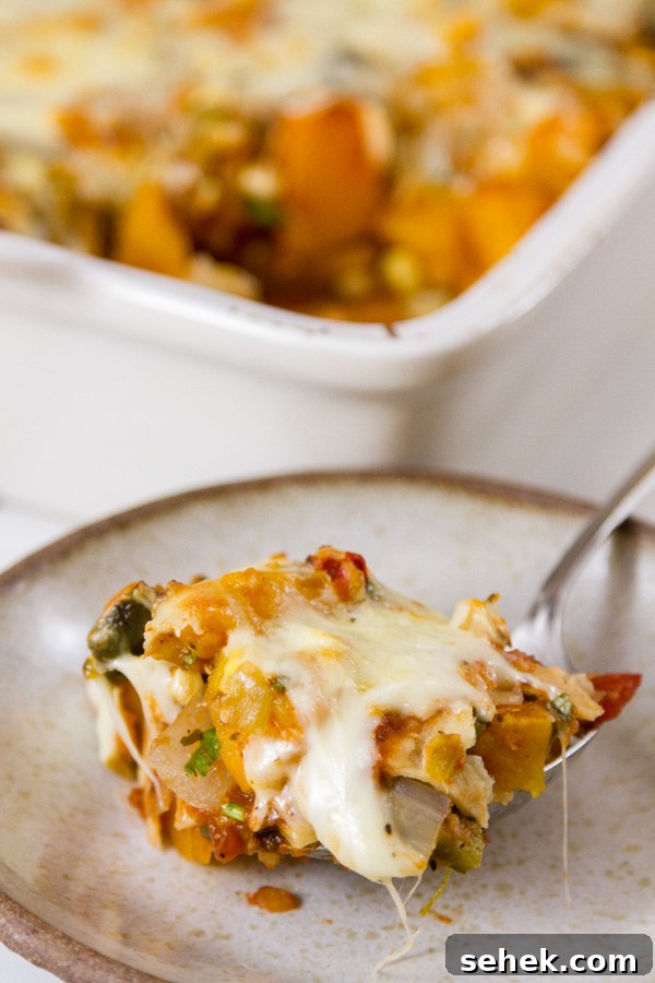 Mexican-Style Butternut Squash Casserole with Chipotle and Cheese 4 serving up a portion of butternut squash casserole onto a smaller plate with the casserole dish in the background