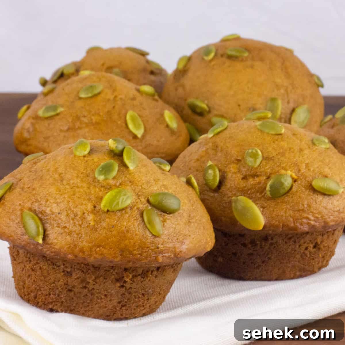Five muffins that are topped with pepitas.