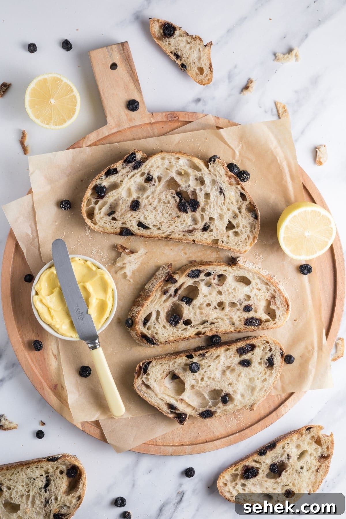 Top Sourdough Bread Add-Ins to Boost Flavor and Texture 3 Slices of sourdough lemon blueberry bread on a parchment lined cutting board with a bowl of butter for serving.