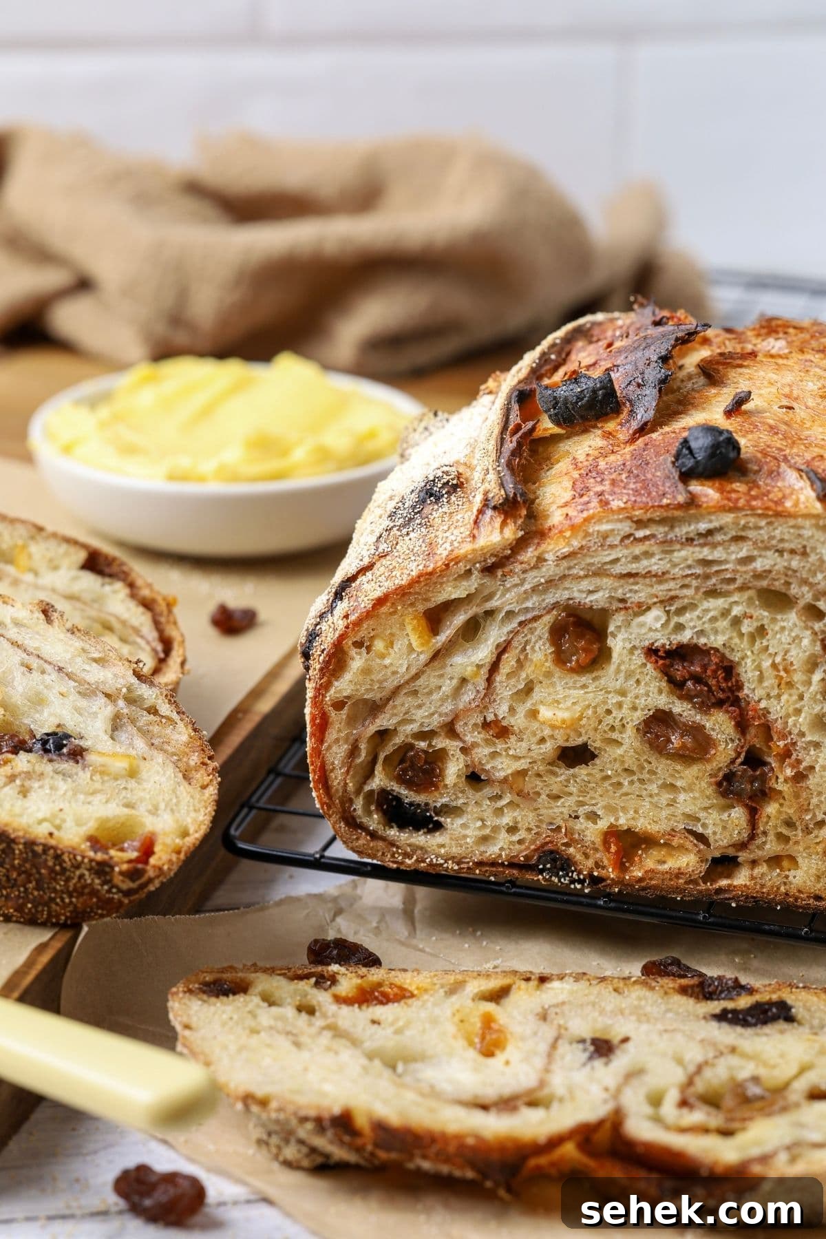 Top Sourdough Bread Add-Ins to Boost Flavor and Texture 5 A sourdough fruit loaf full of juicy raisins and dried fruit sitting on a counter top with a dish of butter. The loaf has been cut so you can see the cinnamon swirl and raisins inside.
