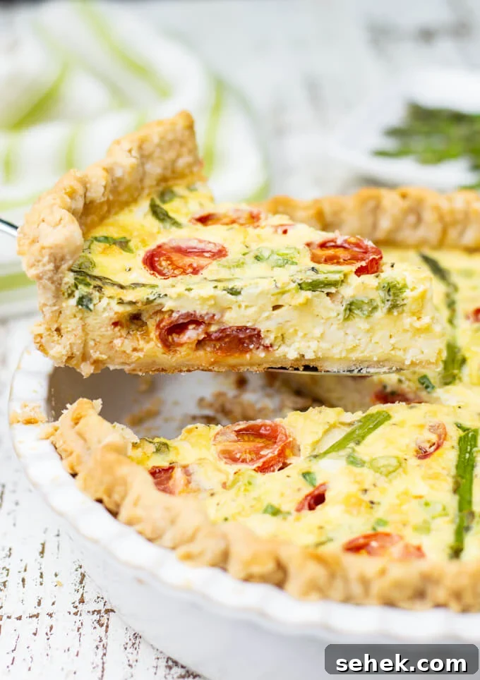 Asparagus and Cherry Tomato Quiche Recipe for Spring Brunch 2 A piece of asparagus quiche with tomatoes is being lifted from the pie plate.