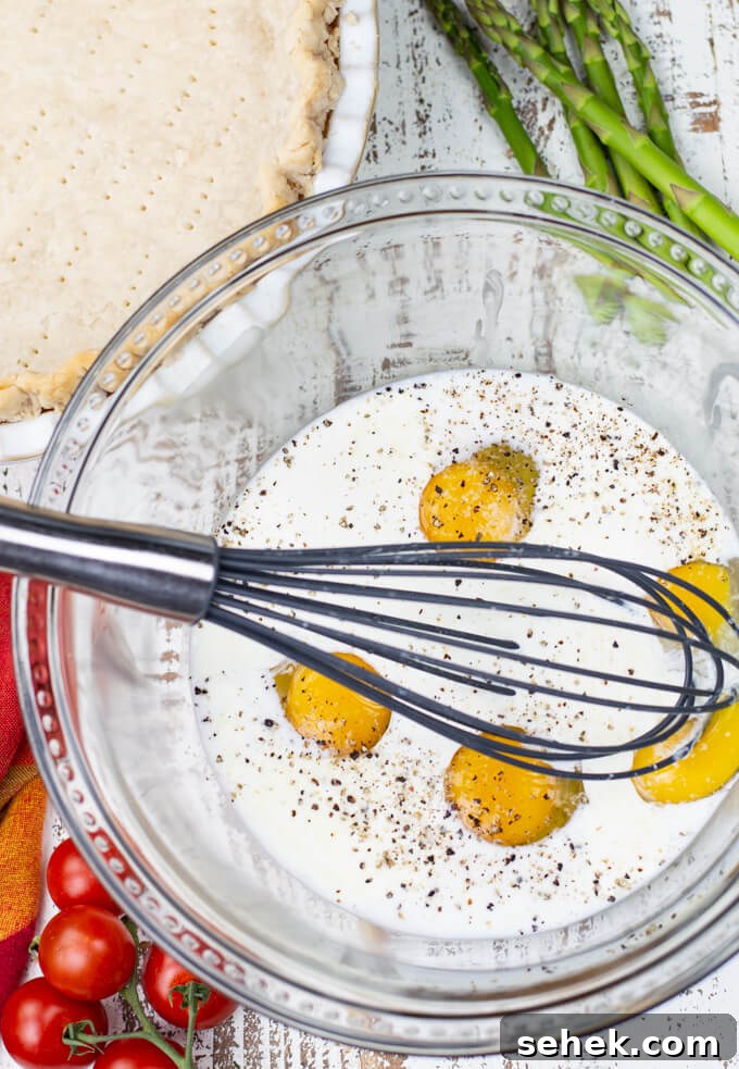 Asparagus and Cherry Tomato Quiche Recipe for Spring Brunch 4 A clear mixing bowl holds cream and eggs and a whisk. A par baked crust , asparagus spears and cherry tomatoes sit next to it.