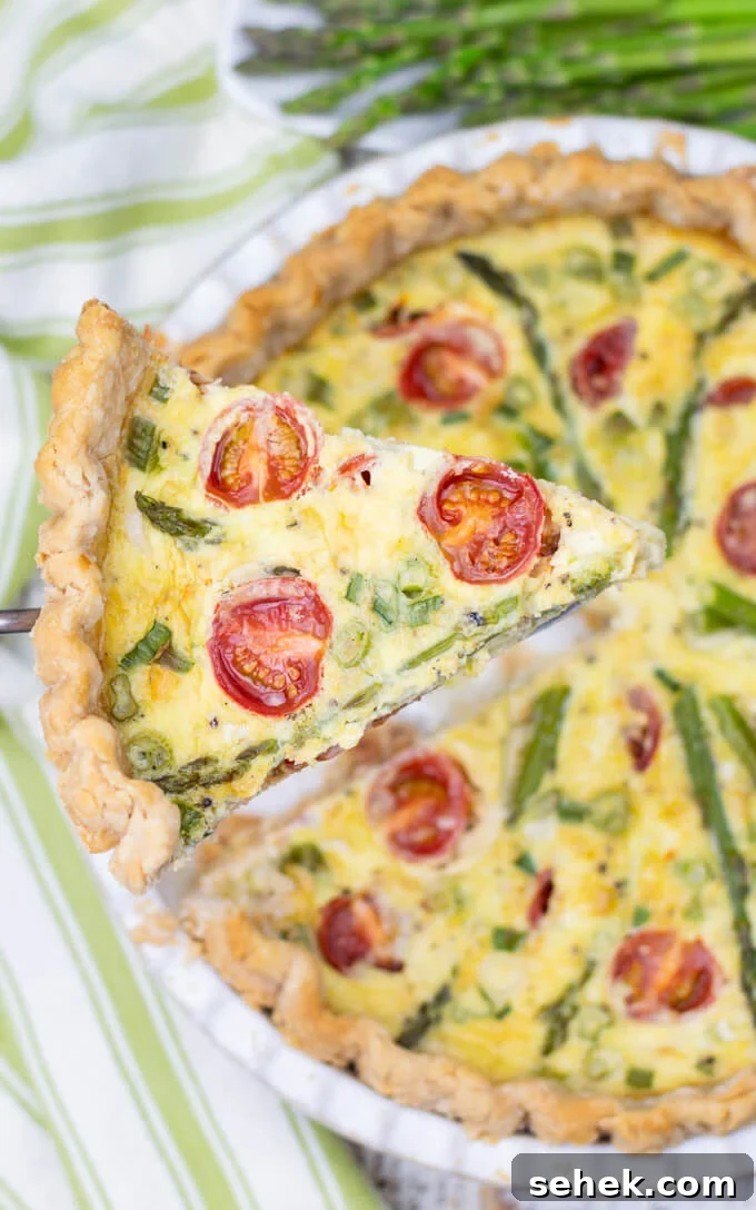 Asparagus and Cherry Tomato Quiche Recipe for Spring Brunch 6 A piece of asparagus quiche with tomatoes is lifted above the pie with a serving utensil. A green napkin rests beside it.
