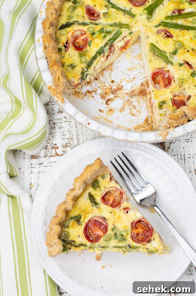 Asparagus and Cherry Tomato Quiche Recipe for Spring Brunch 7 A piece of asparagus quiche with tomatoes sit on a white plate with a fork. A green and white napkin sits next to it with the pie plate of quiche also.