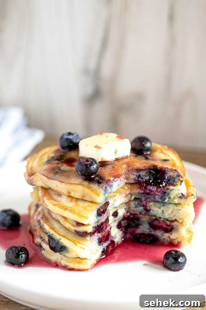 Fluffy Blueberry Pancakes (Made with Frozen Berries) 3 Blueberry Buttermilk Pancakes served with blueberries and syrup and cut up ready to eat.