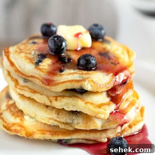 Fluffy Blueberry Pancakes (Made with Frozen Berries) 7 Fluffy Blueberry Pancakes Stacked up and drizzled with blueberry syrup.