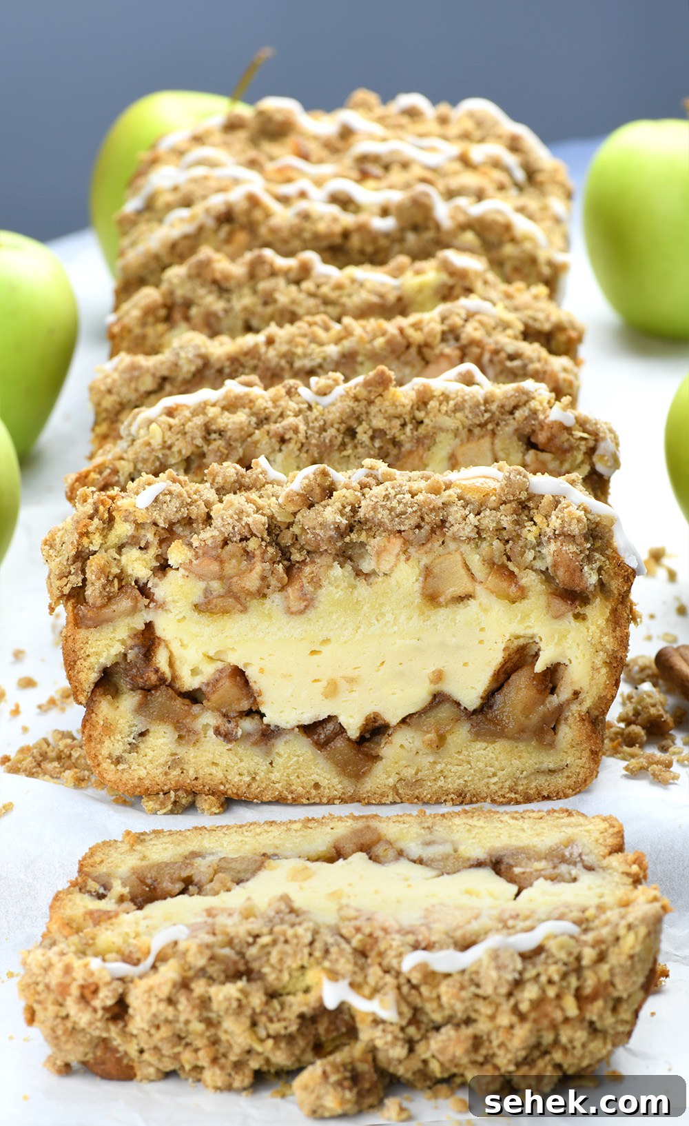 Apple Crisp Cheesecake Bread Recipe — Decadent Fall Dessert 2 Slices of Apple Crisp Cheesecake Bread on a white parchment paper with bunch of green apples.