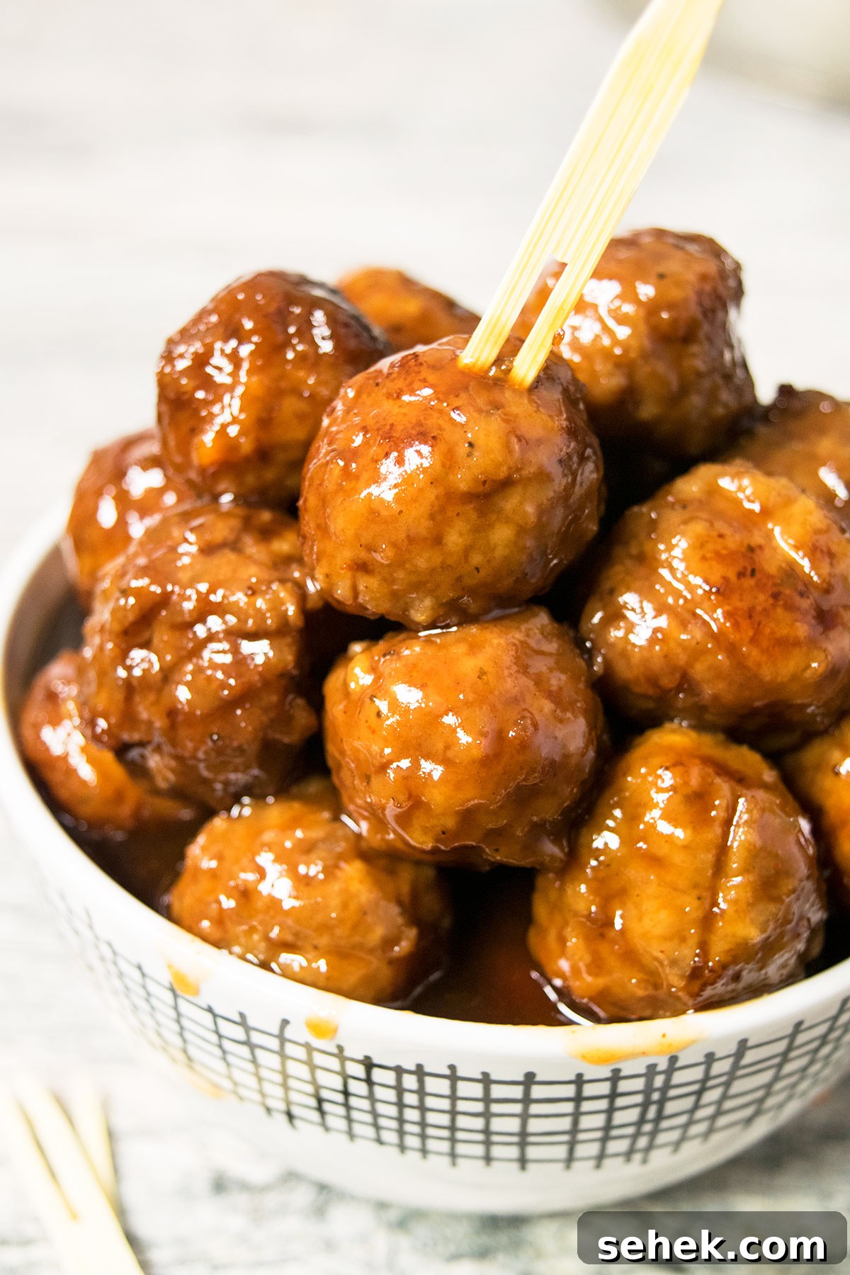 White bowl filled with cocktail meatballs with sauce dripping on the sides.