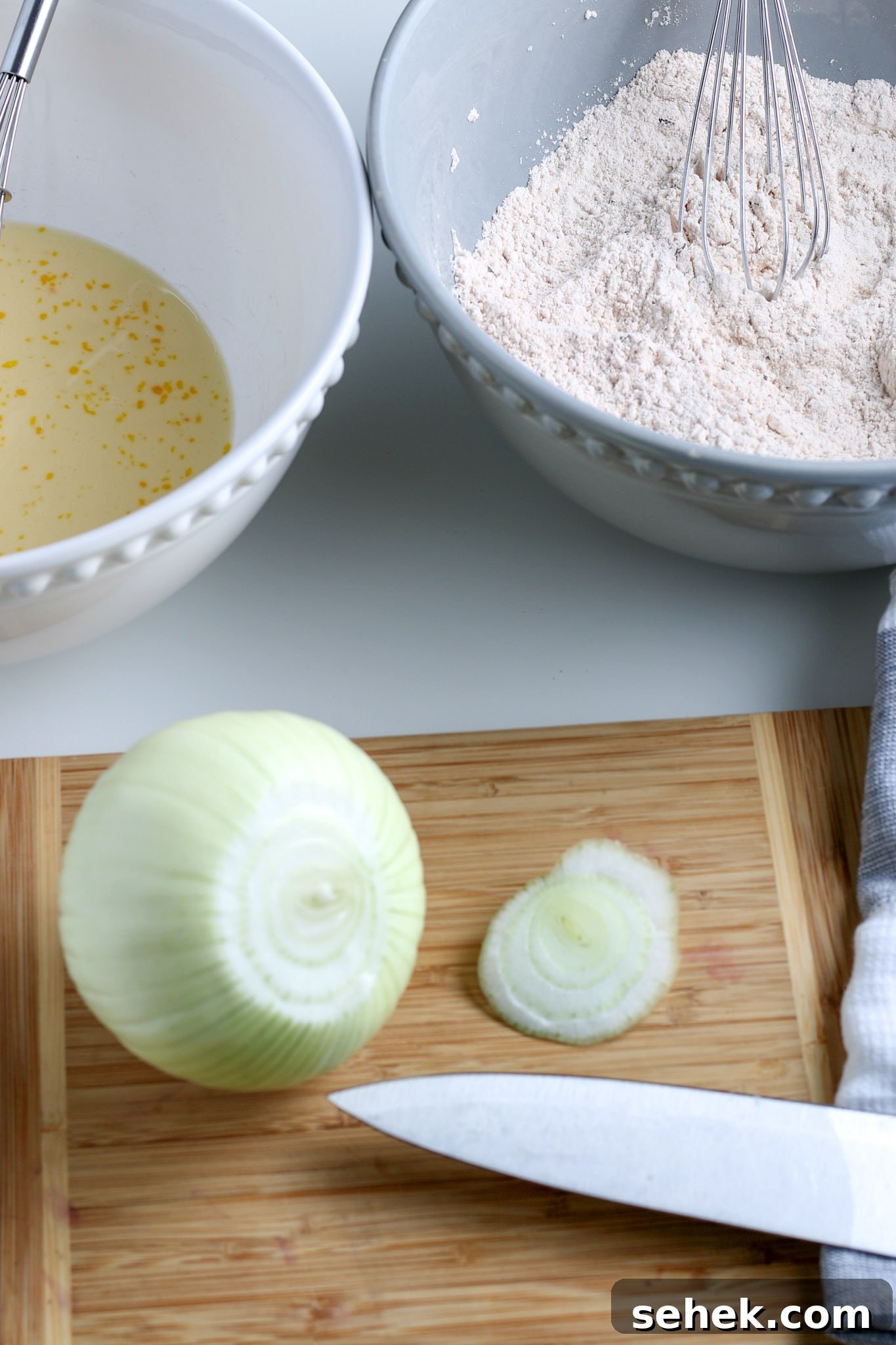 Crispy Air Fryer Blooming Onion Recipe for Perfect Appetizers 4 a large onion on a cutting board with the top cut off, with egg wash and a flour mixture in the background