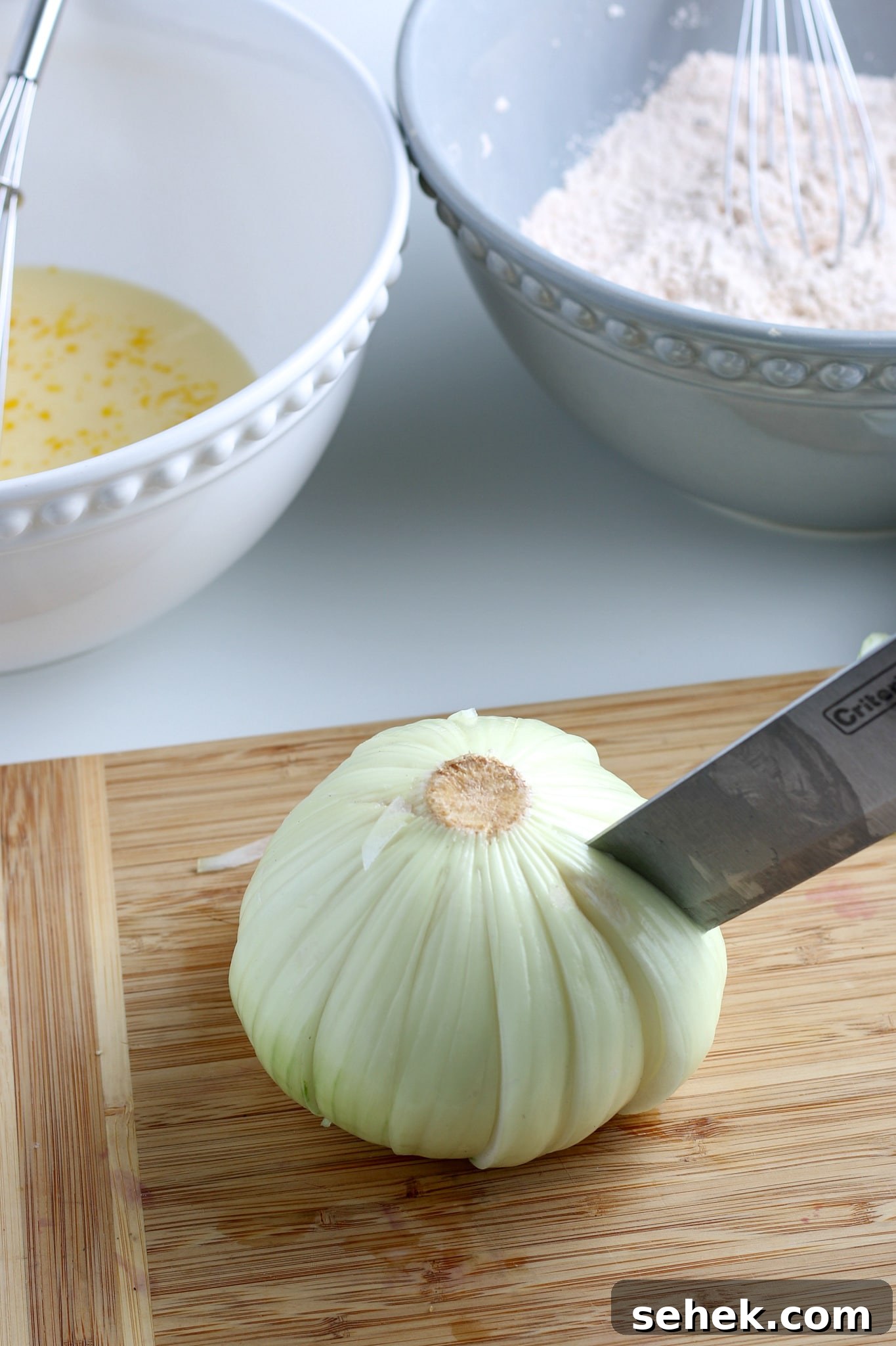 Crispy Air Fryer Blooming Onion Recipe for Perfect Appetizers 6 raw onion being cut into a bloom on a cutting board with two bowls in the background.
