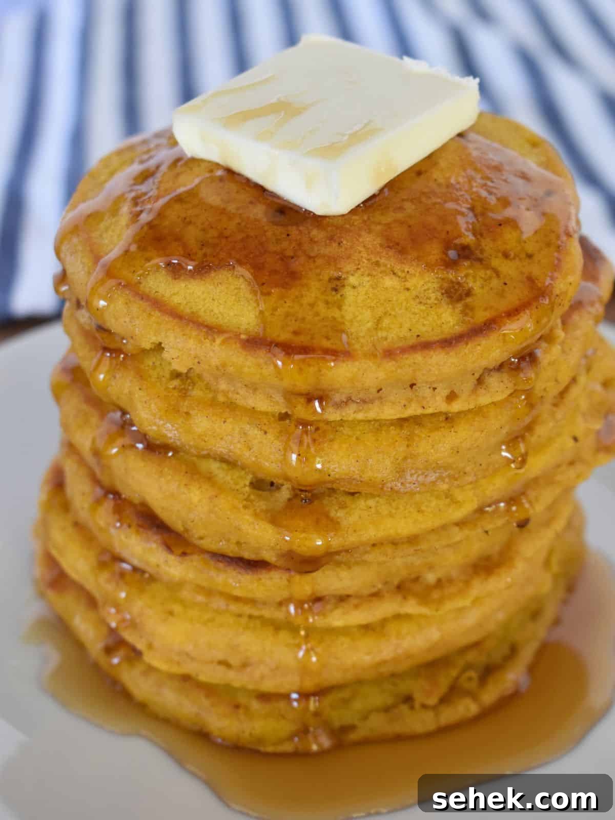 Fluffy Pumpkin Pancakes Using Pancake Mix – Quick Fall Recipe 6 Pumpkin Pancakes with Pancake Mix stacked on a white plate with a striped napkin in the background.