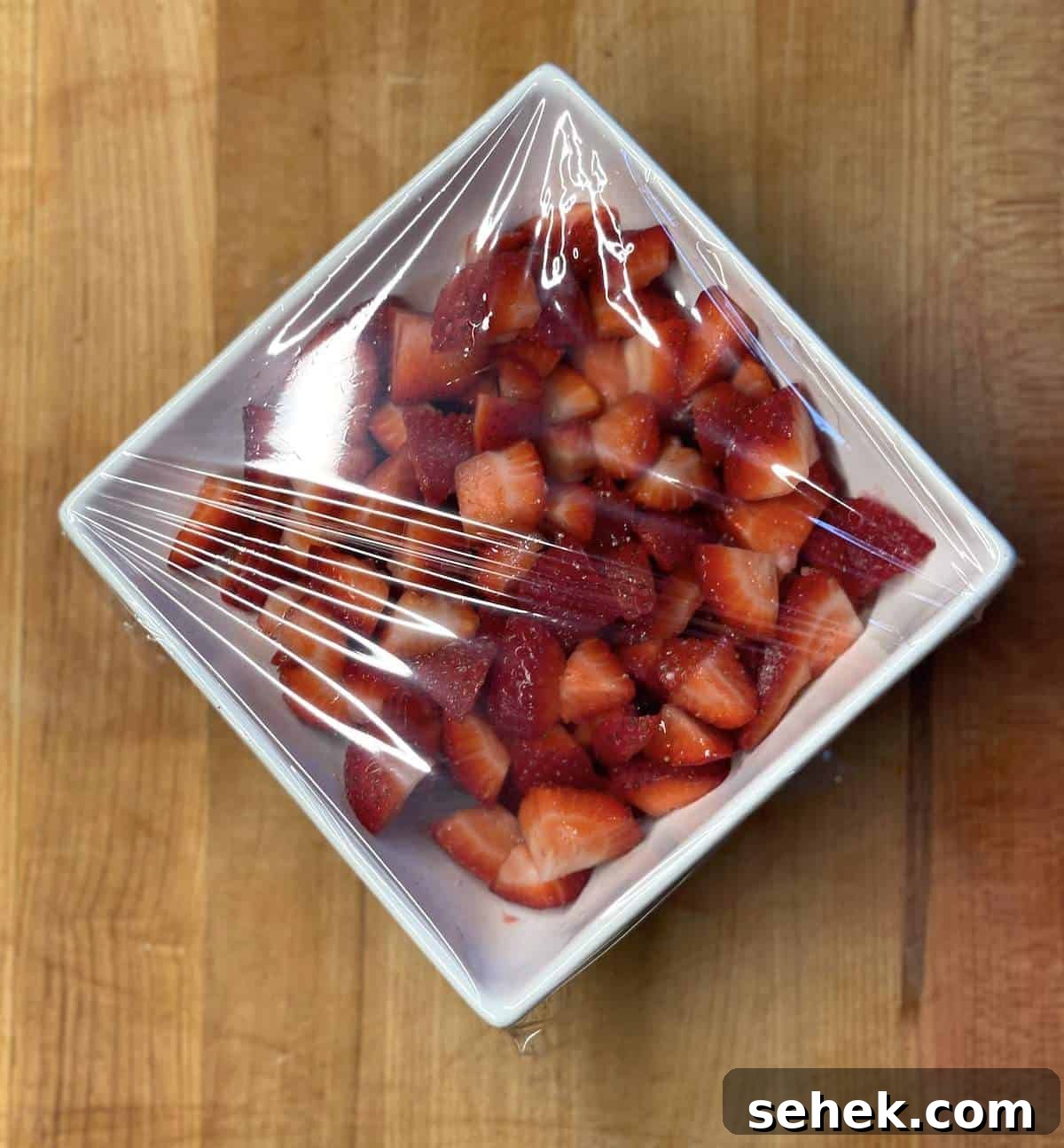 Strawberry Angel Food Shortcake with Fresh Whipped Cream 6 A bowl of sugar coated strawberries wrapped in plastic.
