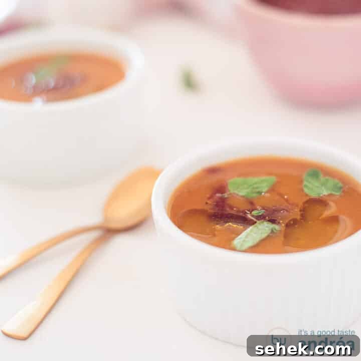 A square photo with a bowl of spicy pumpkin soup. A second one comes diagonally behind it. Two golden spoons to the left.