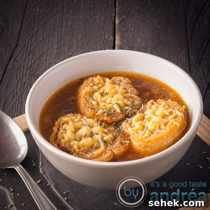 A square photo with a black background on top of a black plate with a bowl filled with onion soup and baguette au gratin with cheese. A spoon on the left
