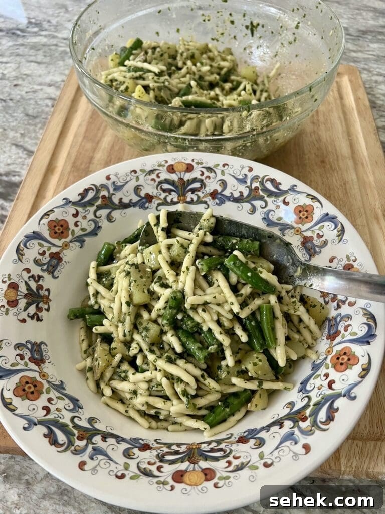 Trofie al Pesto Genovese with Potatoes and Green Beans 14 Spooning finished trofie al pesto genovese into serving bowl with large stainless steel spoon.