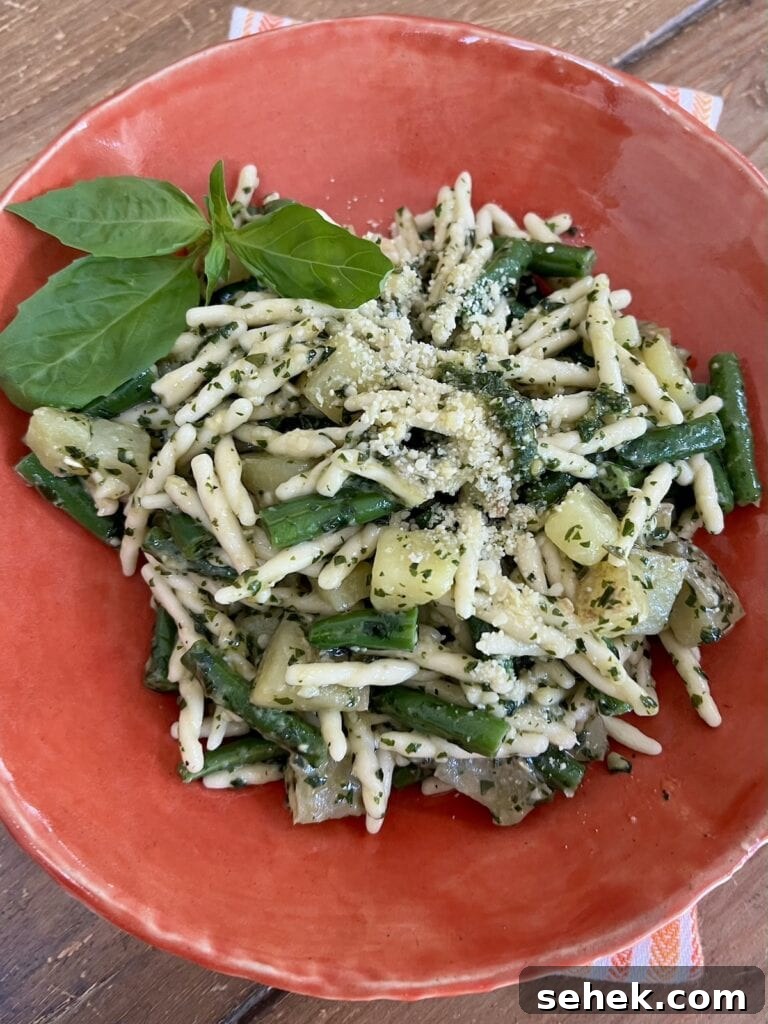 Trofie al Pesto Genovese with Potatoes and Green Beans 3 Pasta with pesto green beans and potatoes in orange bowl with basil sprig garnish and grated cheese.