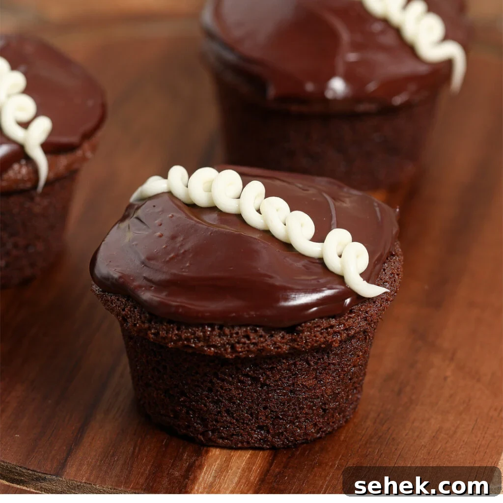 Copycat Little Debbie Oatmeal Creme Cupcakes Recipe 3 Three homemade Little Debbie Cupcakes with glossy chocolate frosting and a white icing swirl on top, arranged on a wooden surface.