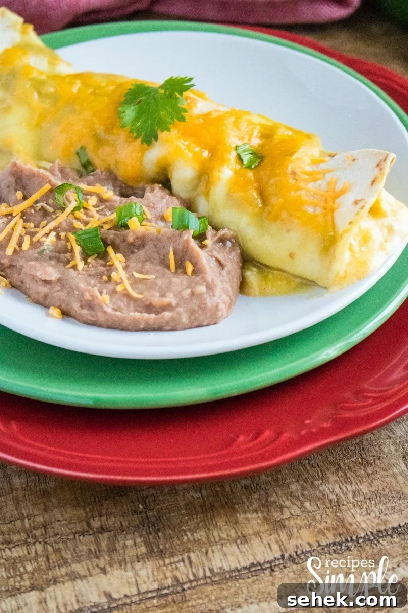 Creamy Cheesy Chicken Enchiladas with Melted Mexican Cheese 6 Baked chicken enchilada on white plate with a side of refried beans.