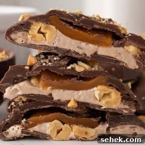 Homemade Snickers bites are stacked and cut in half, revealing the layered interior of chocolate, nougat, caramel, and nuts.