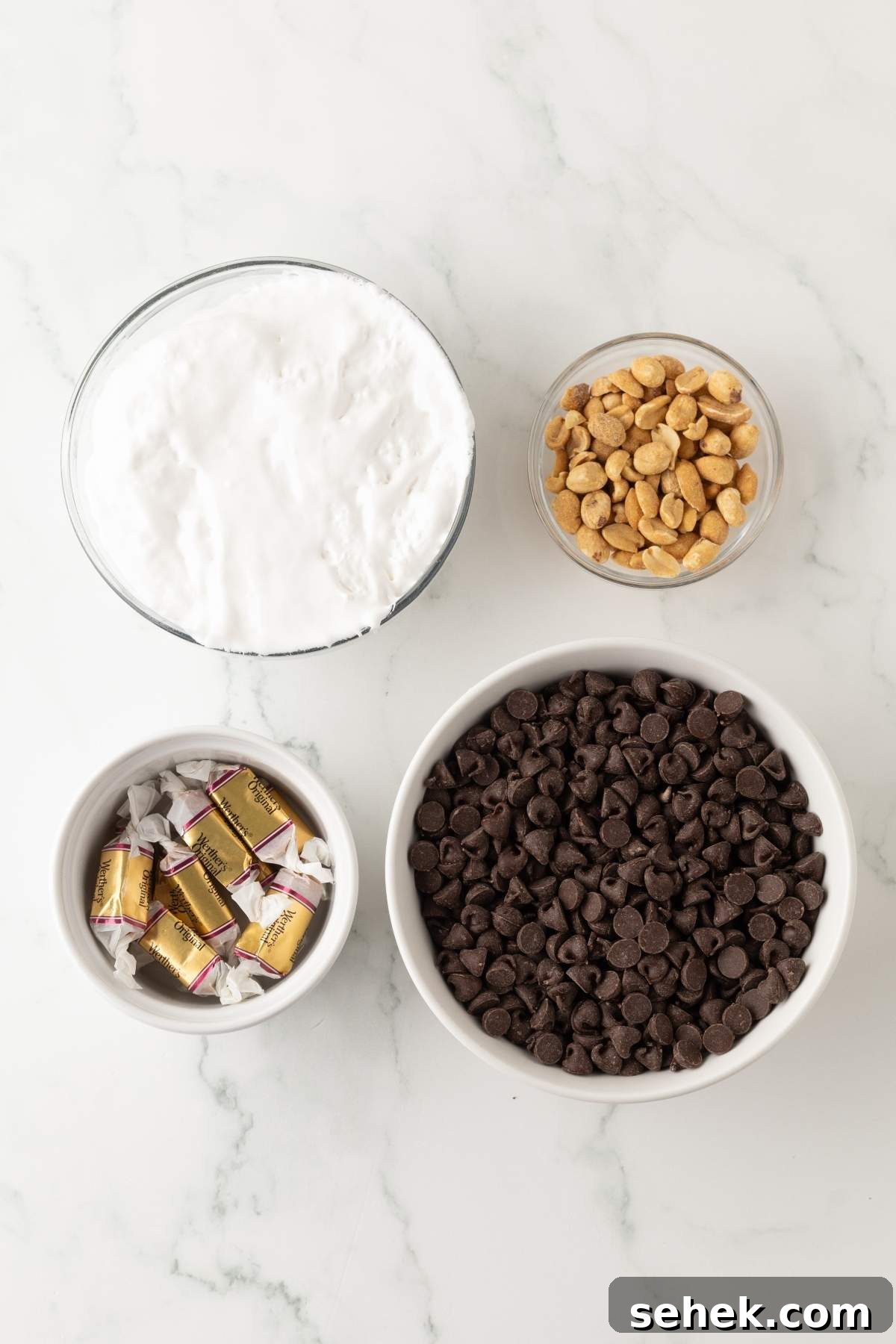 Bowls of whipped cream, peanuts, chocolate squares, and chocolate chips on a marble surface come together to create delightful homemade Snickers bites.