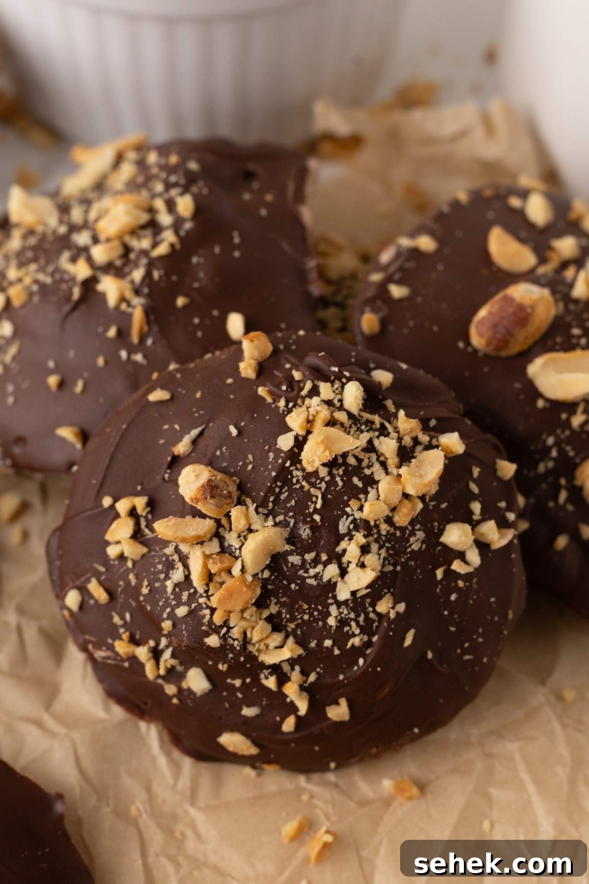 Close-up of three chocolate-covered treats garnished with crushed nuts on parchment paper, reminiscent of homemade Snickers bites.