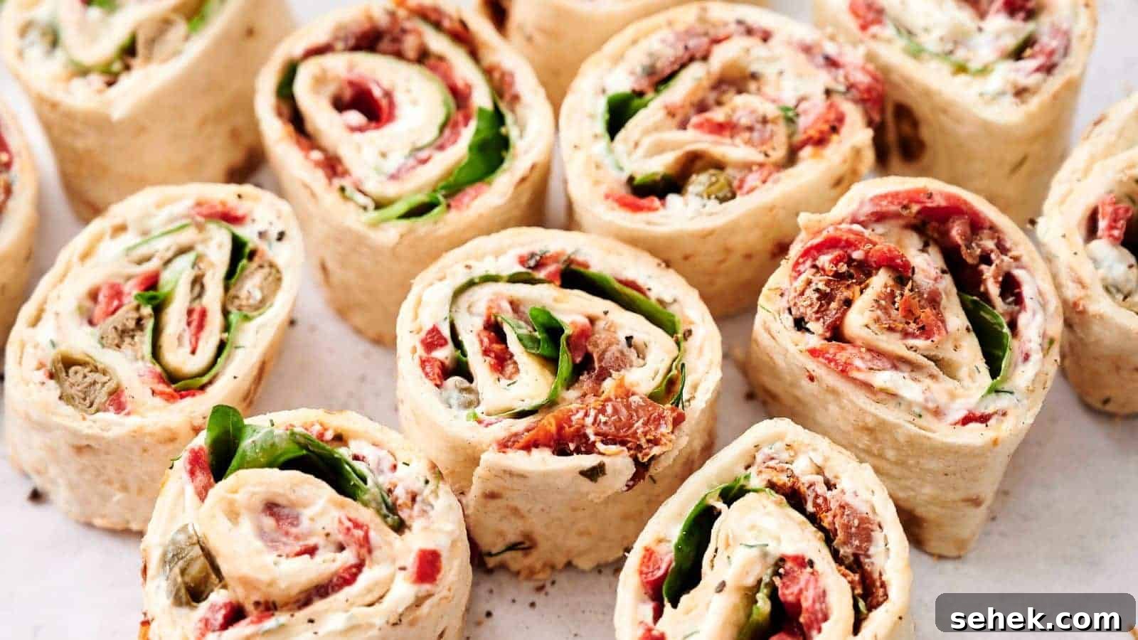 9 Pinwheel Recipes Guests Always Request Again 8 Close-up of several tortilla pinwheel wraps filled with various ingredients including spinach, cream cheese, tomatoes, and other vegetables, arranged neatly on a white surface.