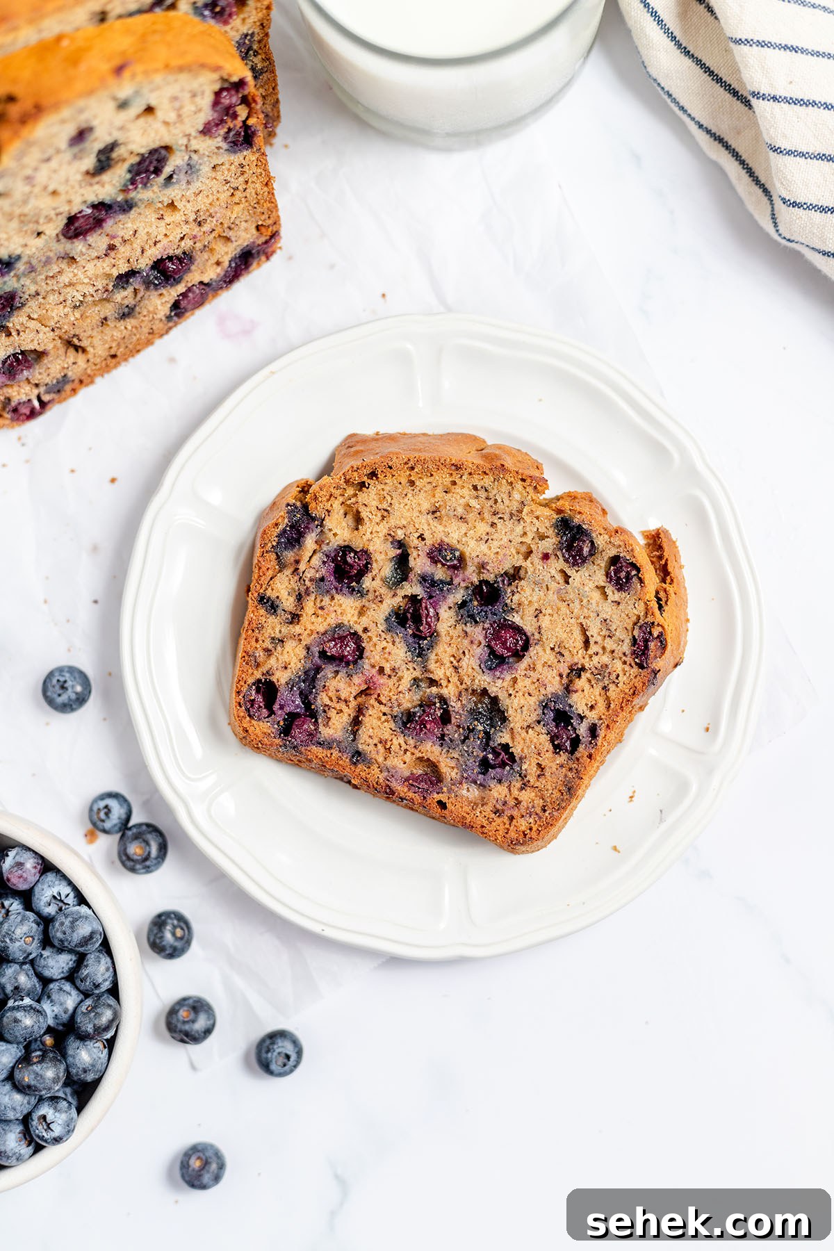 Moist Blueberry Banana Bread Recipe with Lemon Glaze 5 A slice of Blueberry Banana Bread on a white plate.