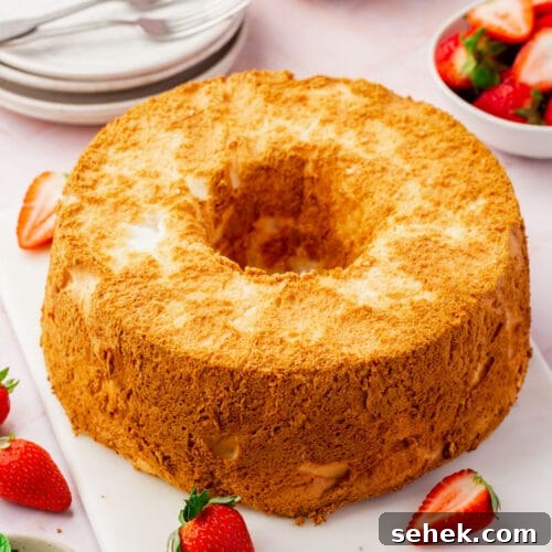 Light and Fluffy Gluten-Free Angel Food Cake Recipe 7 A gluten-free angel food cake on a marble board with fresh strawberries, a bowl of mint leaves and a bowl of whipped cream.