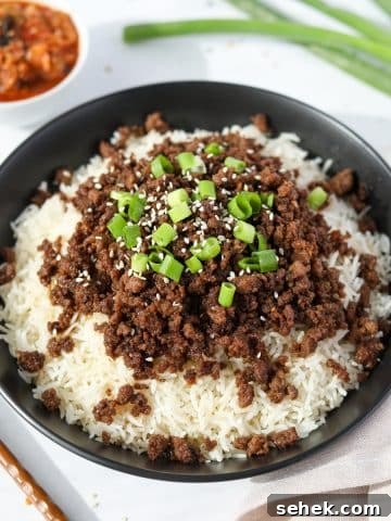 A bowl of rice topped with Korean ground beef, green onions, and sesame seeds.