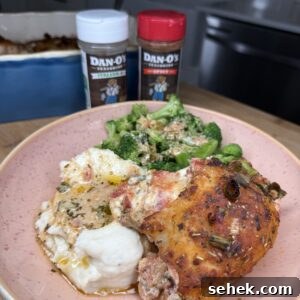 Fire-Roasted Stuffed Chicken Thighs with Herb Cheese Filling 29 A plate of Fire Roasted Stuffed Chicken Thighs, mashed potatoes with gravy, and steamed broccoli sits on a pink dish. Two Dan-O’s seasoning bottles and a casserole dish are visible in the background.