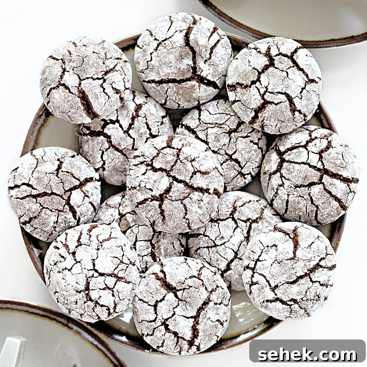 Closeup of cracked tops of powdered sugar covered almond flour chocolate cookies with chocolate cookie dough showing through the cracks.