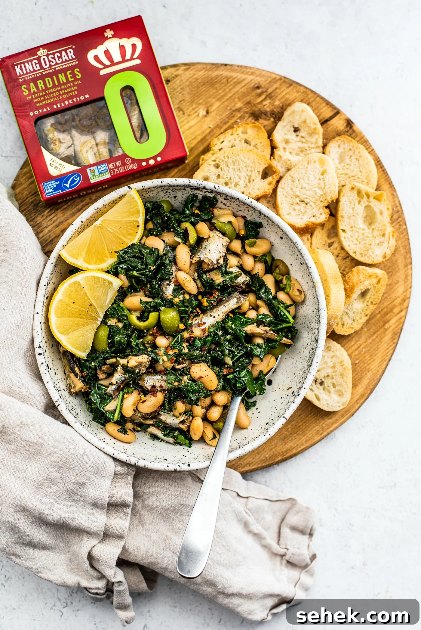 Sauteed Greens and White Beans with King Oscar Sardines 2 Serving board with bowl of greens and beans, toasted baguette slices, and a package of King Oscar sardines.