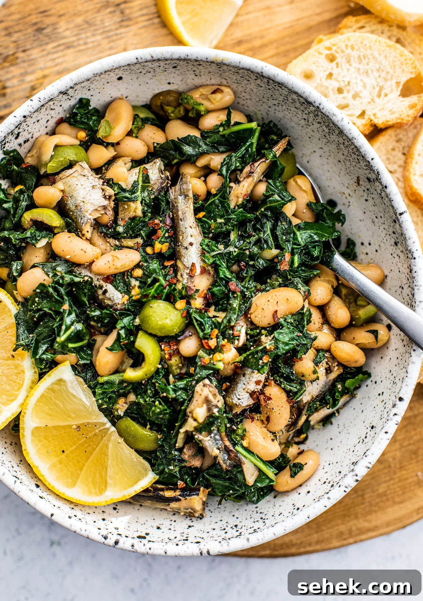 Sauteed Greens and White Beans with King Oscar Sardines 4 Serving bowl full of sauteed kale, white beans, sardines, and lemon wedges.