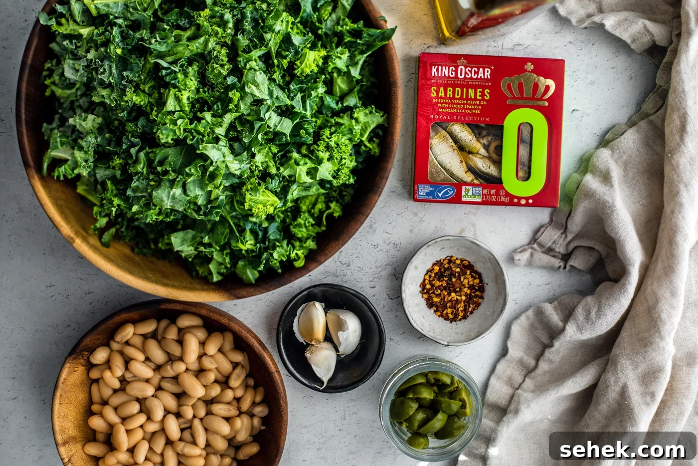 Sauteed Greens and White Beans with King Oscar Sardines 5 Big bowl of chopped kale, bowl of cannellini beans, garlic cloves, chili flakes, and olives next to a container of King Oscar sardines.