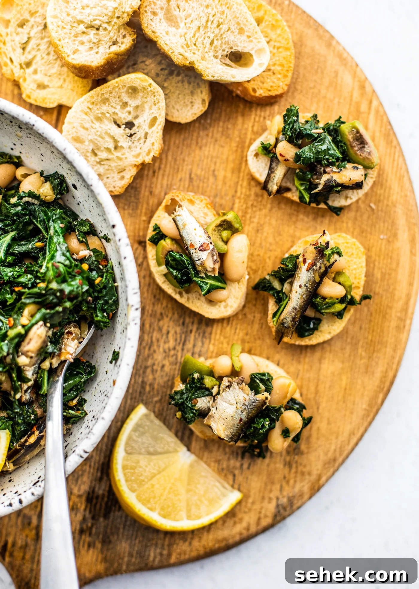 Sauteed Greens and White Beans with King Oscar Sardines 6 Serving board with baguette slices topped with beans and greens, and a bowl of beans and greens on the side.
