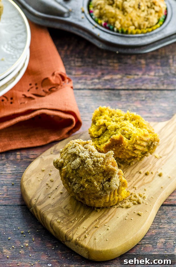 Moist Vegan Pumpkin Muffins with Warm Spices 6 A vegan pumpkin muffin cut in half placed on a small wood cutting board.I In the background there are some white plates stacked placed on top of an orange napkin. On the top right corner there 's the corner of a muffin tin pan with one pumpkin muffin in it