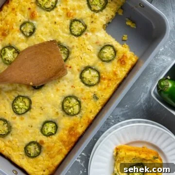 Baked casserole in a baking dish with one serving removed. One serving on a white plate. Wooden spoon resting on top of the casserole.