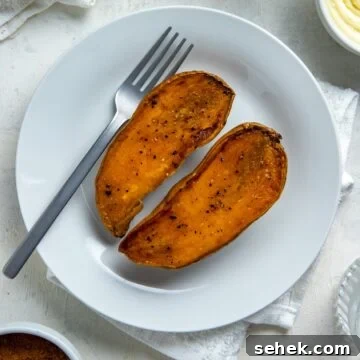 Two roasted sweet potato halves on a round white plate with a fork.
